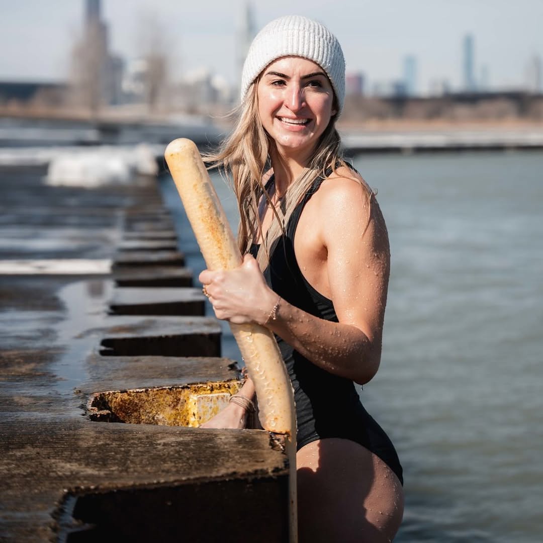 Woman in swimsuit and white beanie smiling after cold water immersion outdoors.